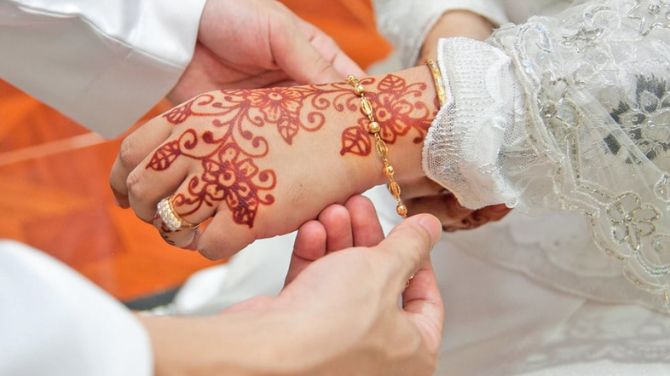 A man and woman holding hands, showcasing intricate henna tattoos, during their nikah ceremony in Makkah.
