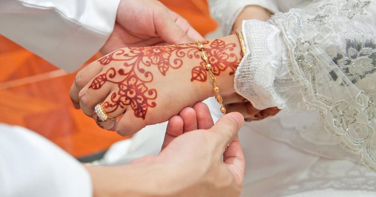 A man and woman holding hands, showcasing intricate henna tattoos, during their nikah ceremony in Makkah.