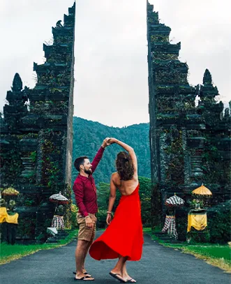 A romantic couple dancing in front of the iconic Handara Gate in Bali with a mountain backdrop.