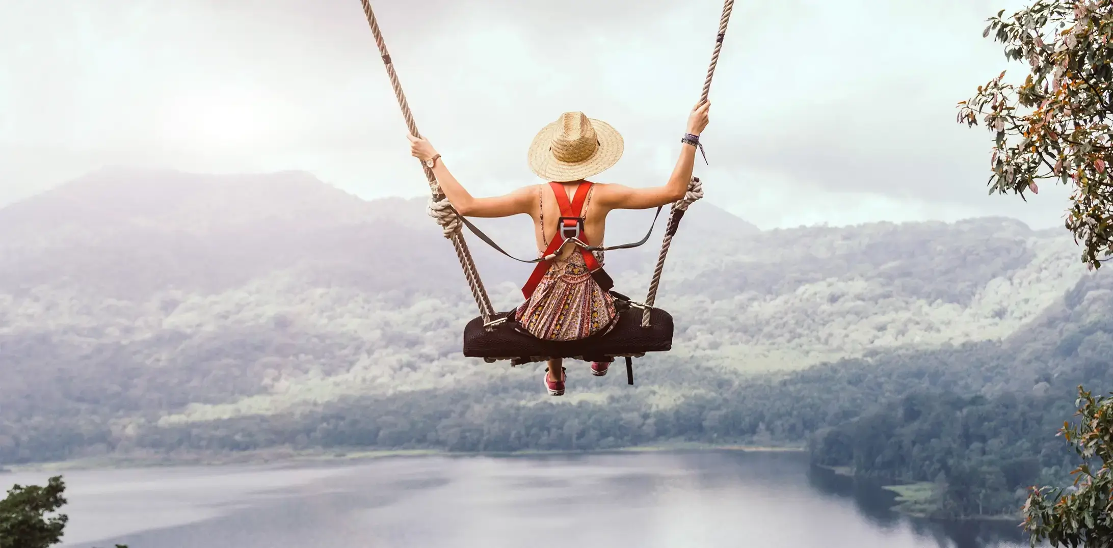 Tourist enjoying a scenic swing adventure overlooking lush green mountains and a beautiful lake in Bali.