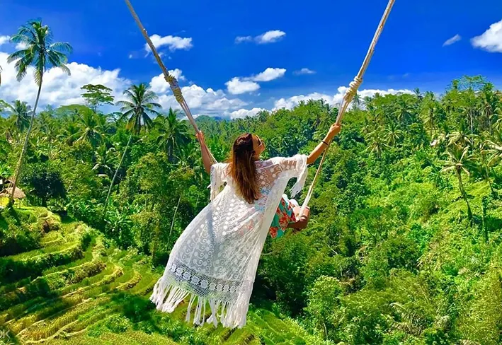 A woman in a white lace dress enjoying the famous Bali swing over lush green rice terraces, a top experience in our bali tour package from kolkata.