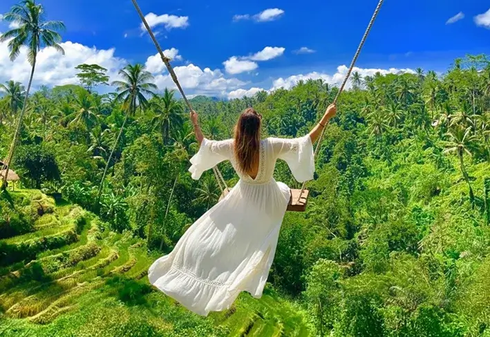 A woman in a white lace dress enjoying the famous Bali swing over lush green rice terraces, a top experience in our bali tour package from kolkata.