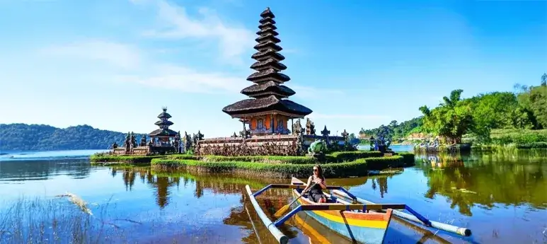 Stunning lake view of a Balinese Hindu temple with a traveler in a colorful boat, perfect for your bali tour package.