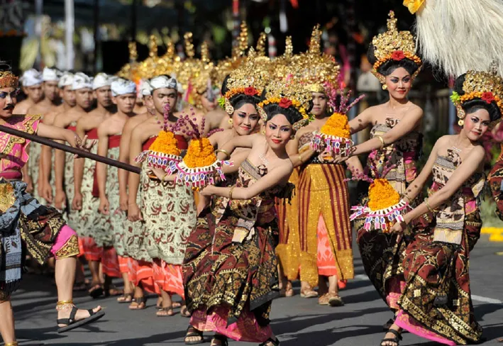 Group of Balinese dancers in traditional golden headdresses and vibrant attire performing at a festival