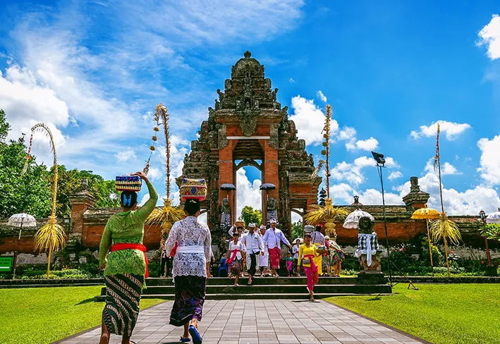 Traditional Balinese devotees walking through the ornate stone gateway of Pura Taman Ayun.