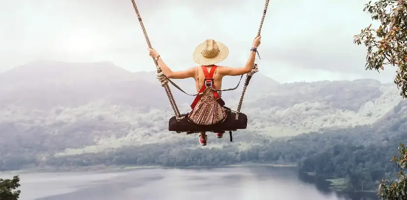 Tourist enjoying a scenic swing adventure overlooking lush green mountains and a beautiful lake in Bali.