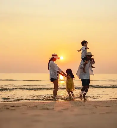 The family enjoys a fun-filled beach vacation at sunset, with parents and two children walking in the water.