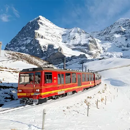 Beautiful winter landscape in Switzerland featuring a red passenger train and snow-capped mountains.