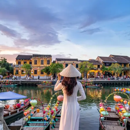 A woman in traditional attire stands on a boat in Hoi An, Vietnam, perfect for an unforgettable international tour package.