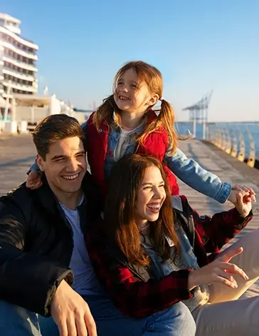 A happy young family smiling together by the waterfront at sunset, a core memory from our Singapore Family Packages.