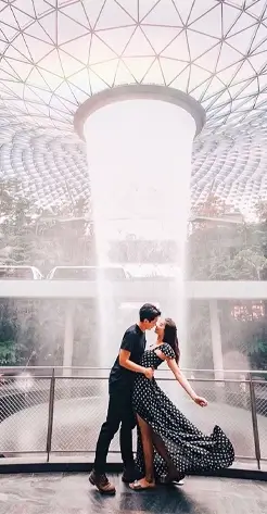 A romantic couple posing in front of the HSBC Rain Vortex at Jewel Changi Airport, a highlight of a Singapore Honeymoon tour.