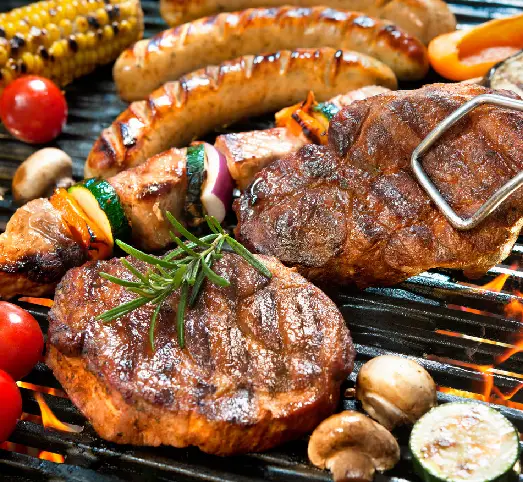 Sizzling grill with assorted meats and vegetables, including steaks, sausages, and skewers, garnished with rosemary—a delicious meal option for the Umrah with Dubai journey.